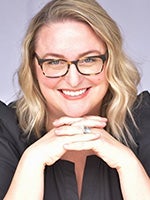 Caitlyn Hart smiles at the camera with hands interlocked under chin